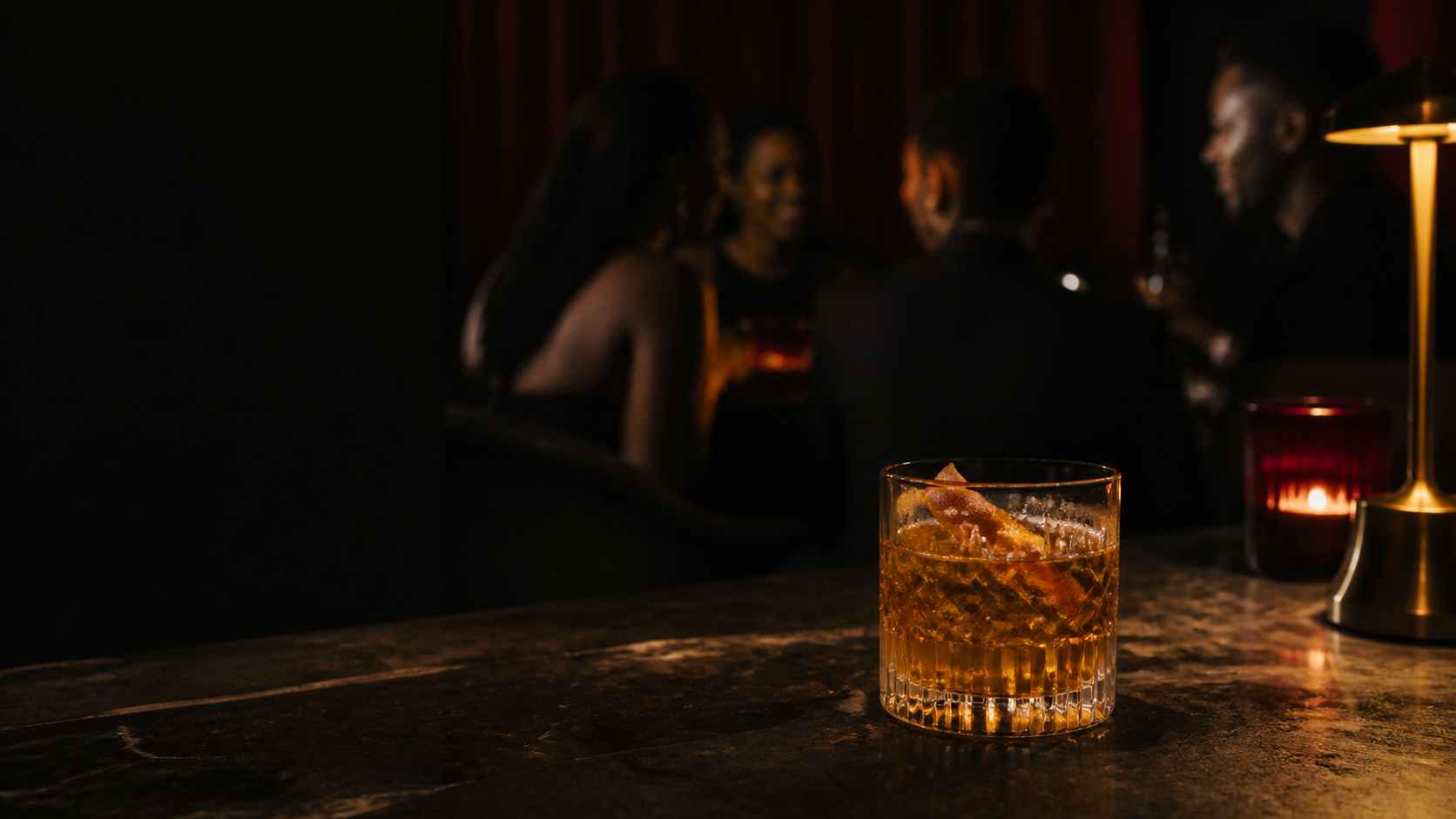 Warm amber drink on a dark bar with a softly lit group in the background